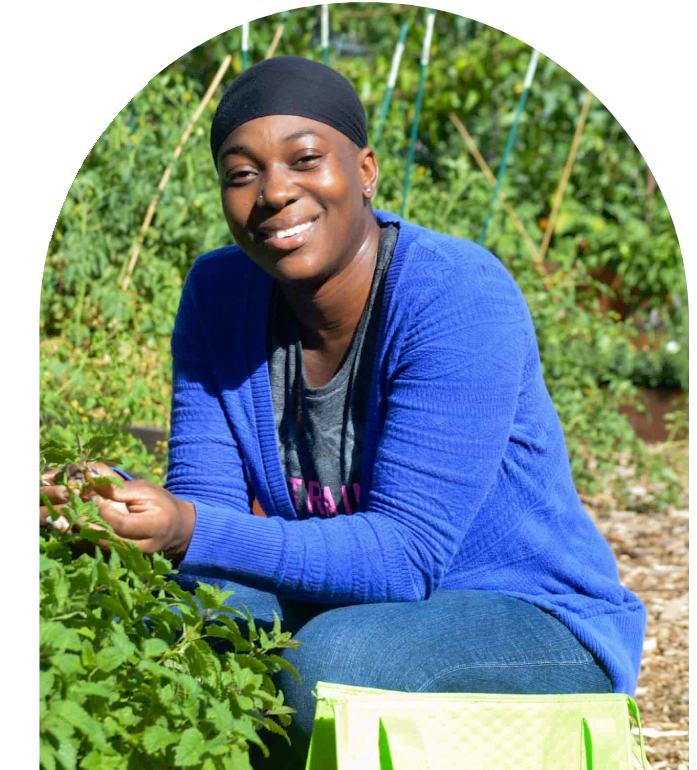 A woman kneeling down in the grass picking vegetables.